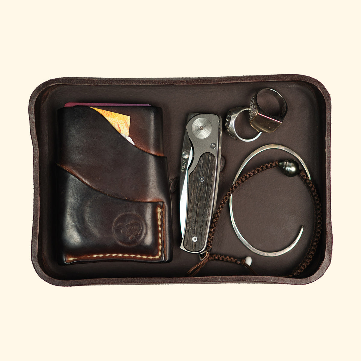 Dunkelbraunes Leder-Tray von oldpassion mit Geldbörse, Messer und Schmuck zur eleganten Organisation von Alltagsgegenständen.